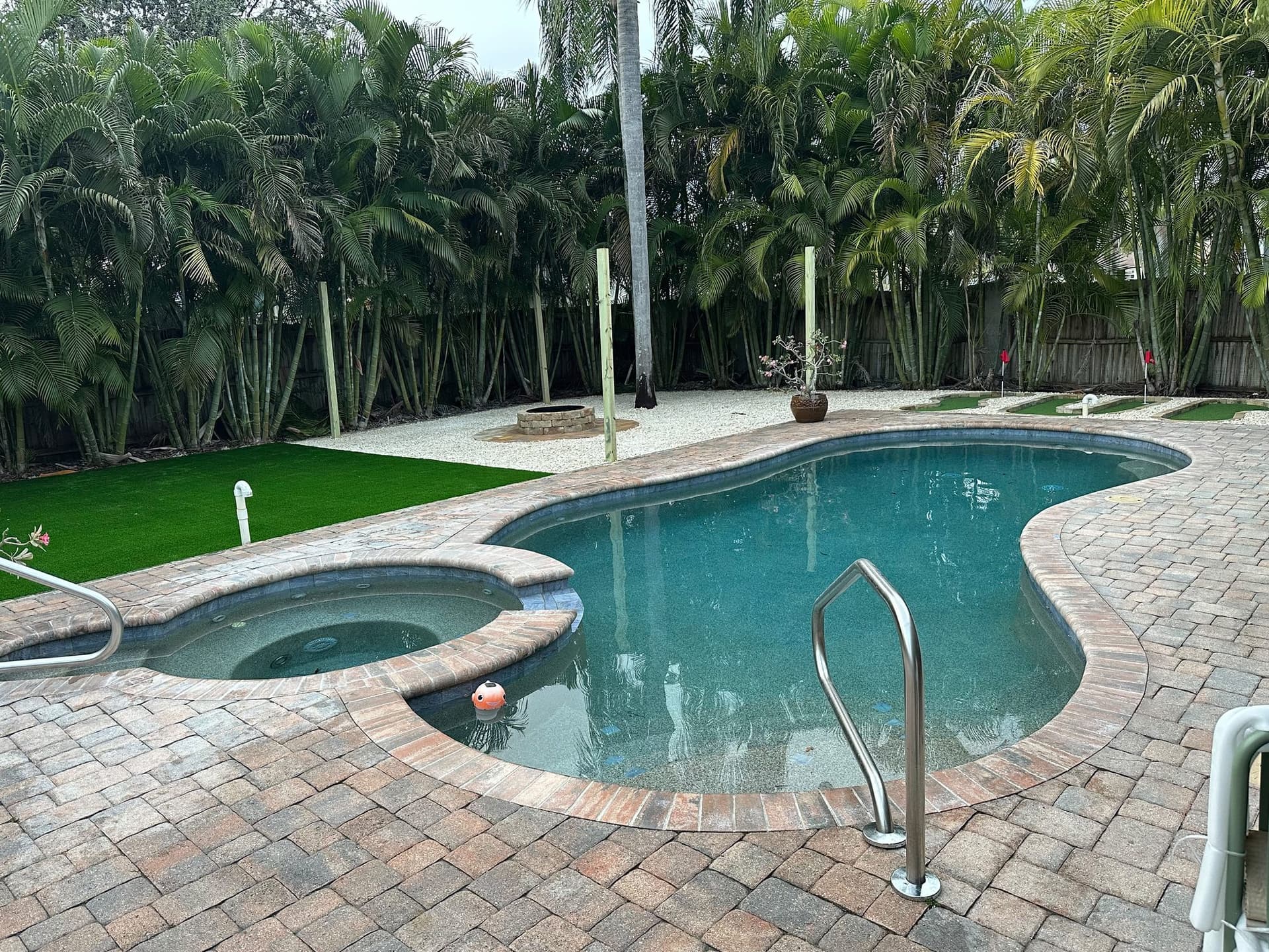 Travertine paver pool deck with a curved pool, spa, and palm trees installed in a Tampa Bay backyard